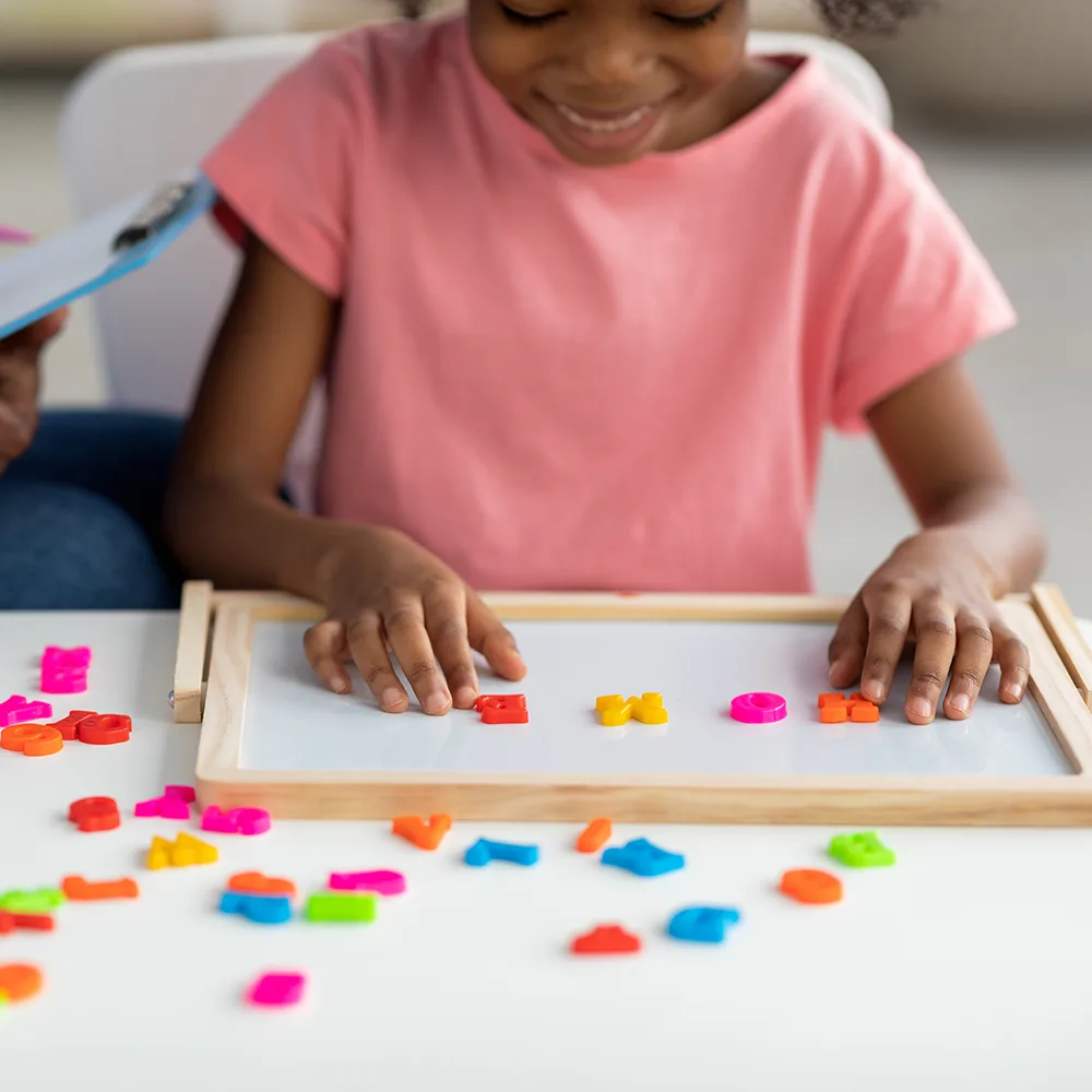A child using magnetized colorful letters to spell HOME at a Red Balloon Child Care Center daycare