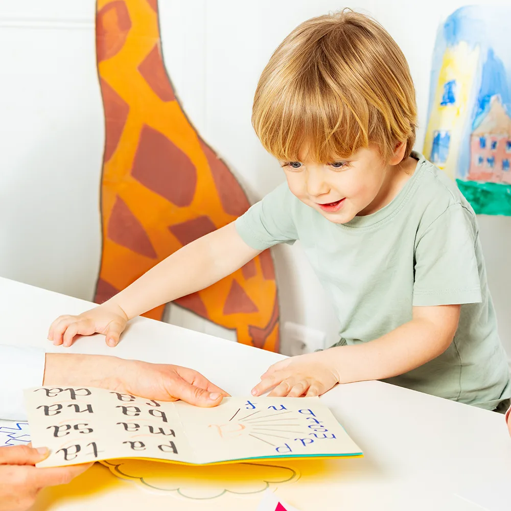 A child smiling and looking at a school book at a Red Balloon Child Care Center daycare
