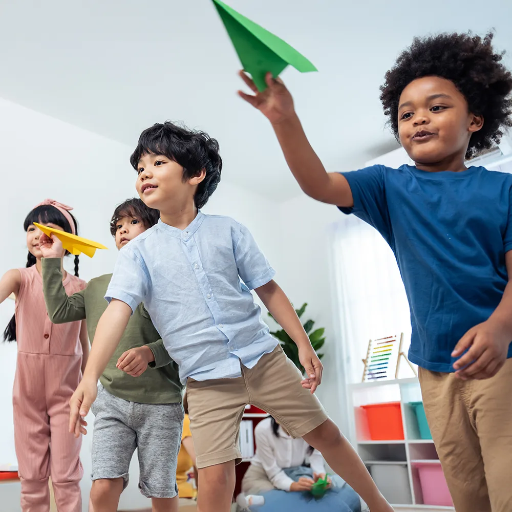 Children launching colorful paper airplanes in a Red Balloon Child Care Center daycare