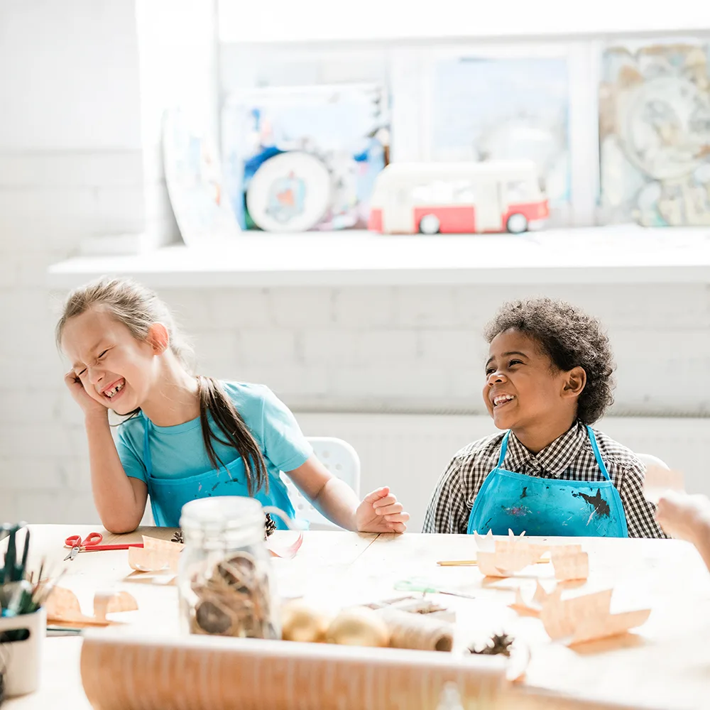 Two children laughing at a table working on crafts at a Red Balloon Child Care Center daycare