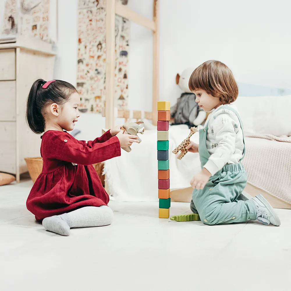 Two children stacking colorful blocks on a floor at Red Balloon Child Care Center daycare