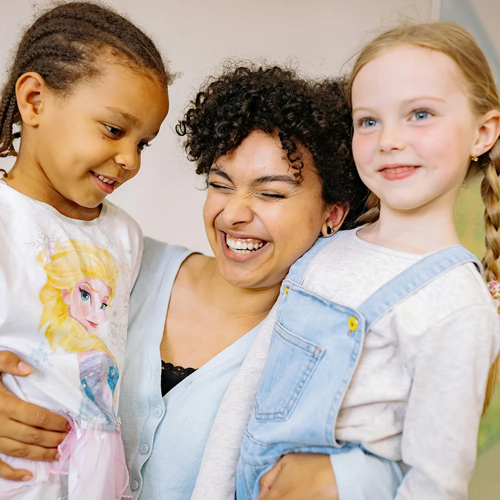 An adult hugging two children and smiling at a Red Balloon Child Care Center daycare