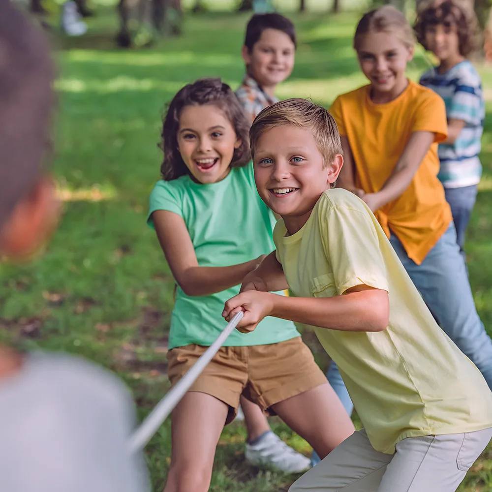 A group of children playing tug of war during summer camp at a Red Balloon Child Care Center daycare