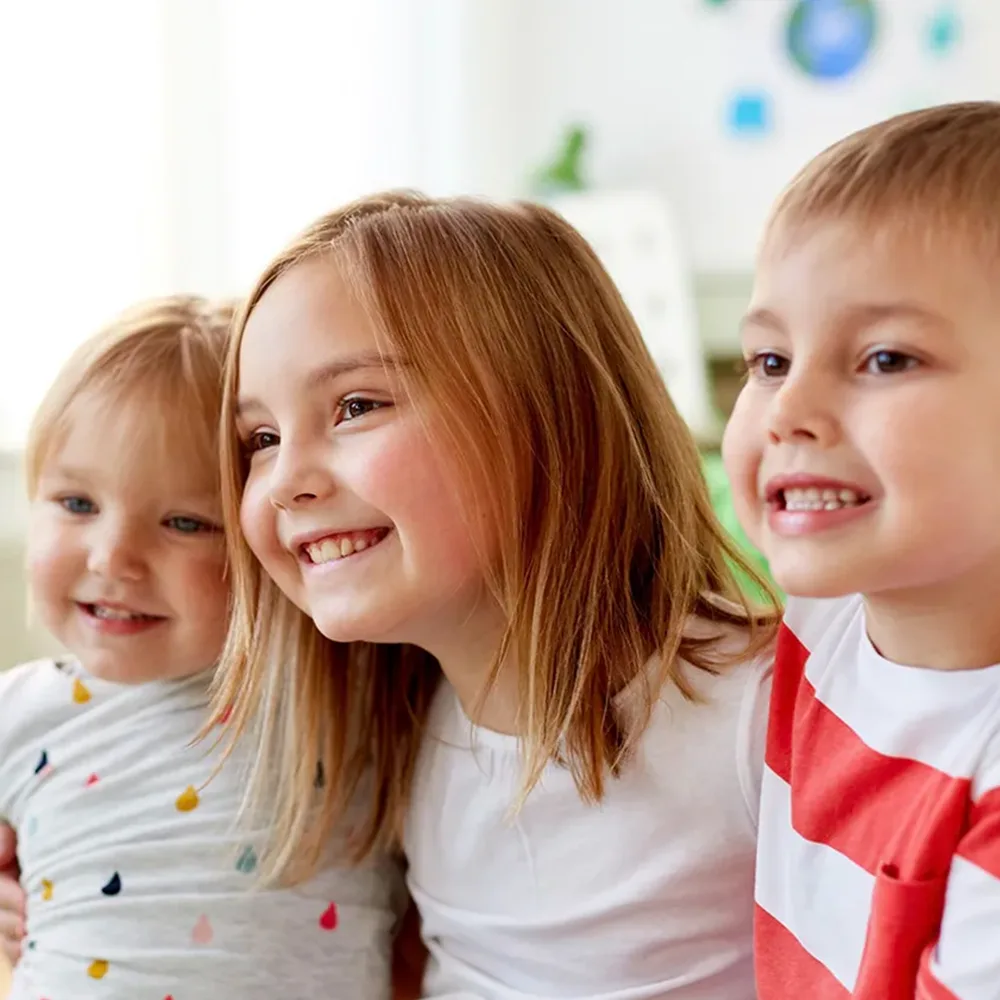 Three children hugging and smiling at a Red Balloon Child Care Center daycare