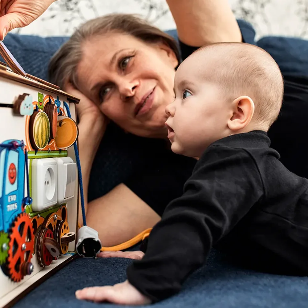 A teacher showing an infant a play box on the floor at a Red Balloon Child Care Center daycare