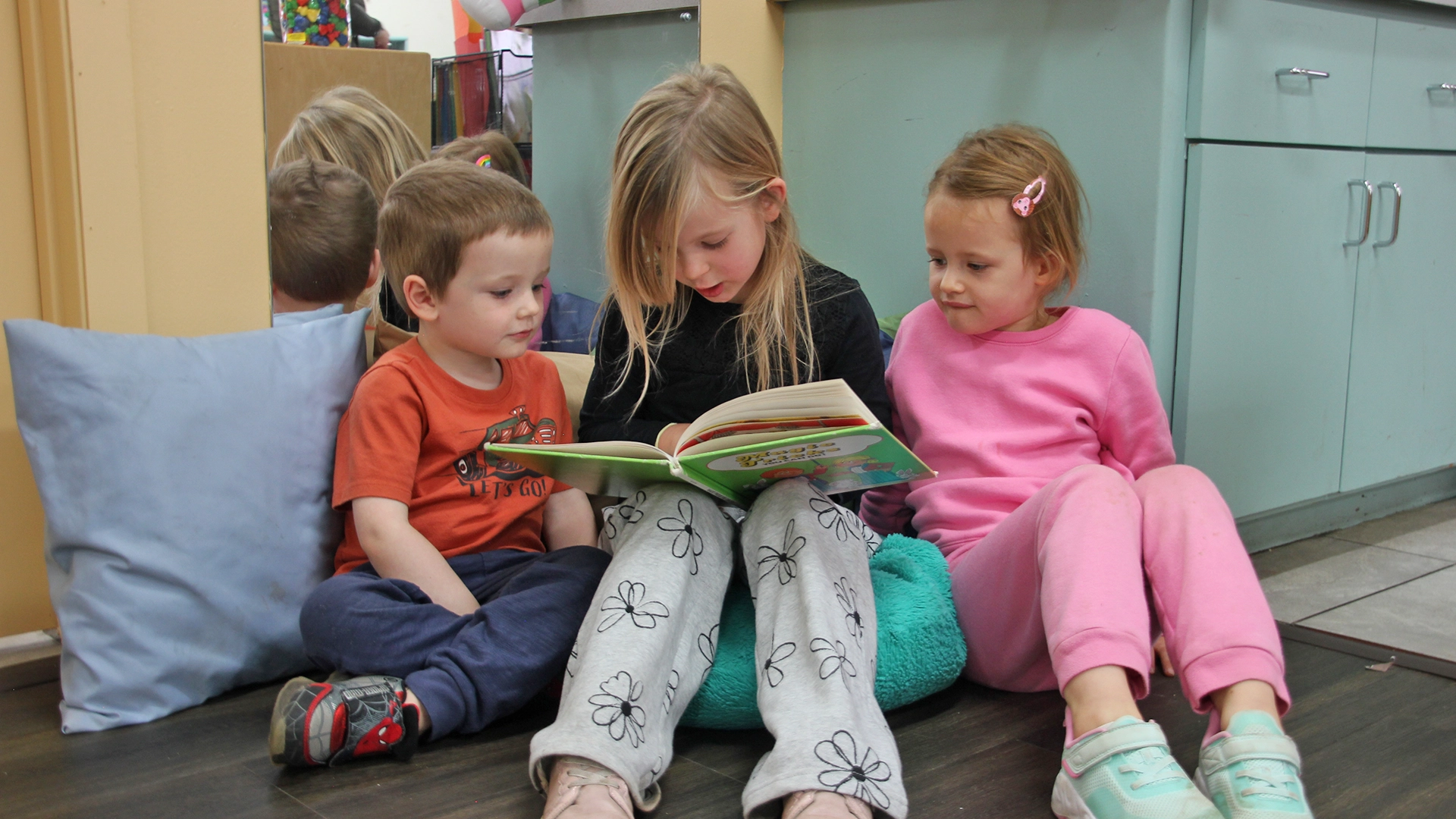 An older child reading a book to two younger children