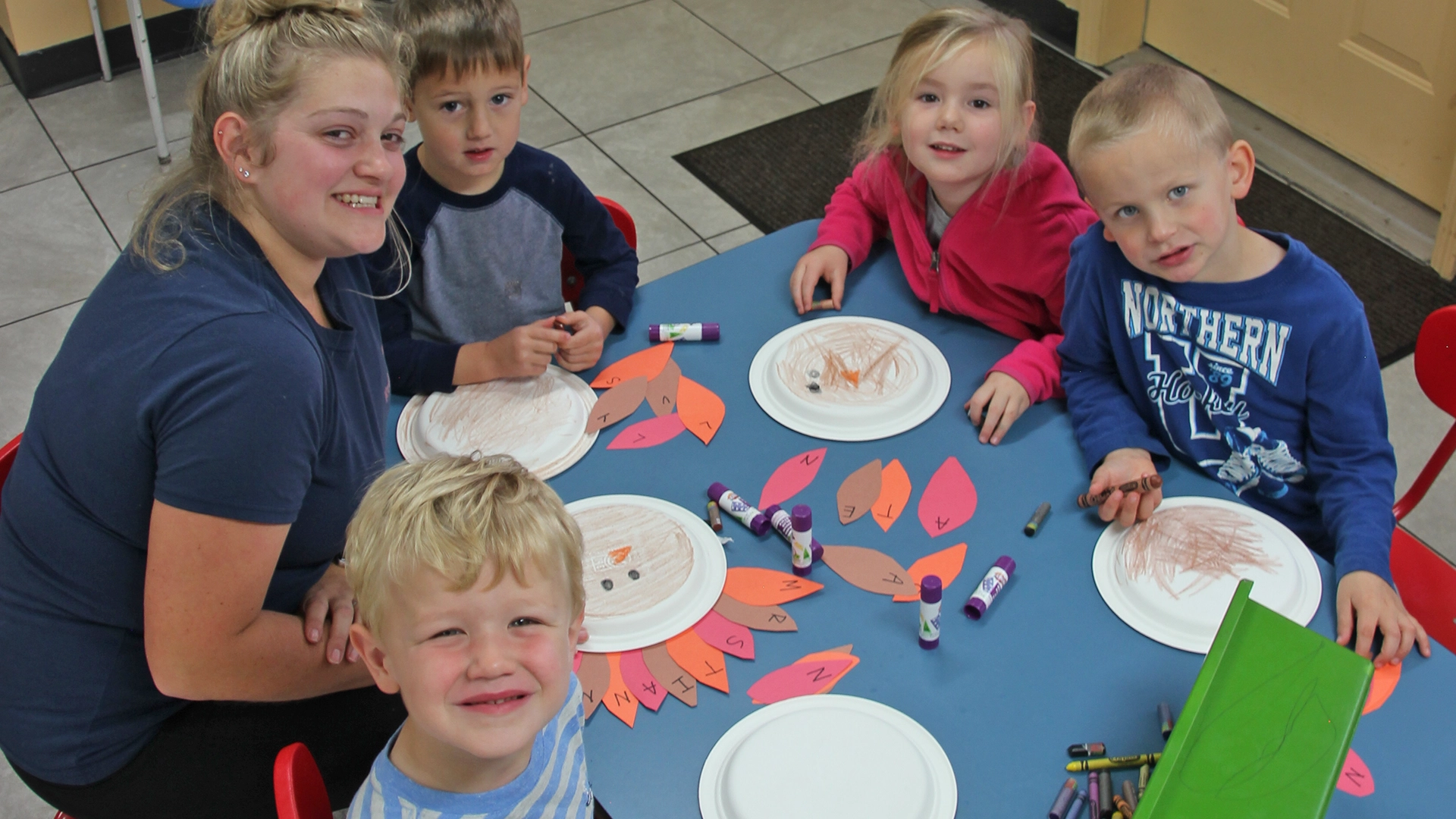 A group of children at a table working on crafts and smiling